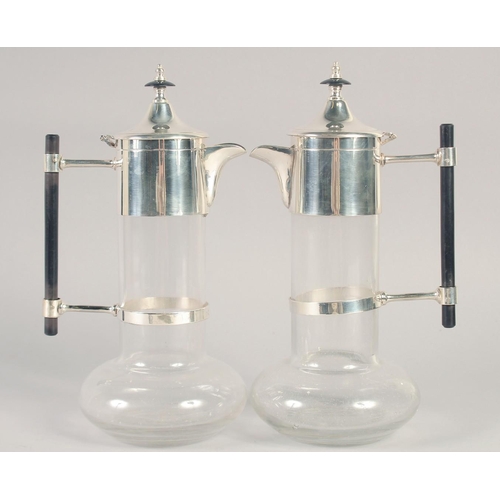 1681 - A GOOD PAIR OF CHRISTOPHER DRESSER STYLE GLASS AND SILVER PLATE CLARET JUGS with ebony handles.