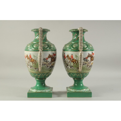 1151 - A PAIR OF SEVRES DESIGN GREEN GROUND HUNTING VASES with looped handles on square bases.