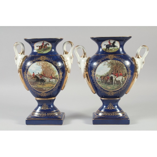 1128 - A PAIR OF CONTINENTAL BLUE TWO HANDLED HUNTING SCENE VASES. 11ins high.