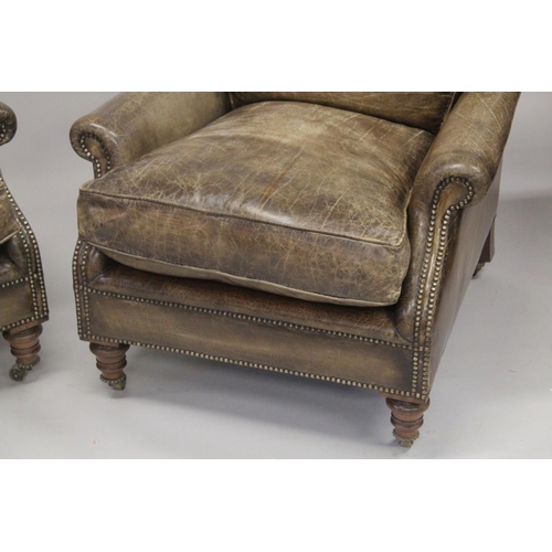 1008 - A SUPERB PAIR OF LEATHER ARMCHAIRS  with brass studs on turned legs, with brass casters. 2ft 8ins wi... 