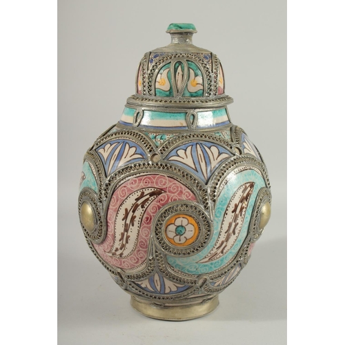 303 - A MOROCCAN METAL MOUNTED POTTERY LIDDED JAR, the jar painted with foliate motifs, 37cm high.