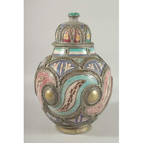 303 - A MOROCCAN METAL MOUNTED POTTERY LIDDED JAR, the jar painted with foliate motifs, 37cm high.