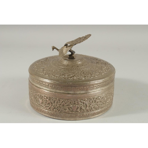 310 - A MALAYSIAN EMBOSSED SILVER CIRCULAR BOX, with figural peacock finial and foliate decoration, 18cm d... 