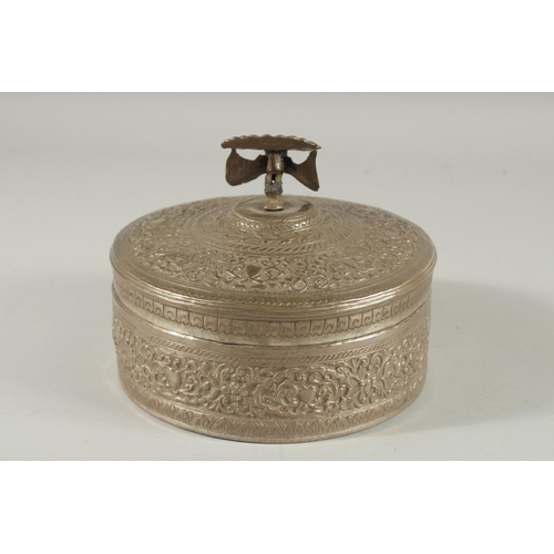 310 - A MALAYSIAN EMBOSSED SILVER CIRCULAR BOX, with figural peacock finial and foliate decoration, 18cm d... 