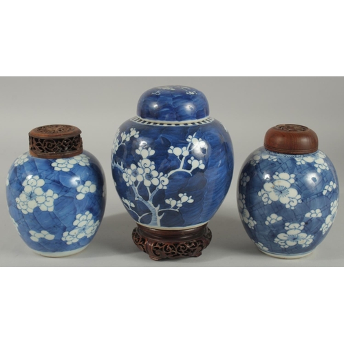 9 - THREE CHINESE BLUE AND WHITE PRUNUS JARS AND COVERS, two with wooden covers and one with wooden stan... 