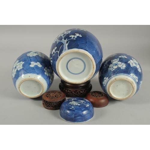 9 - THREE CHINESE BLUE AND WHITE PRUNUS JARS AND COVERS, two with wooden covers and one with wooden stan... 