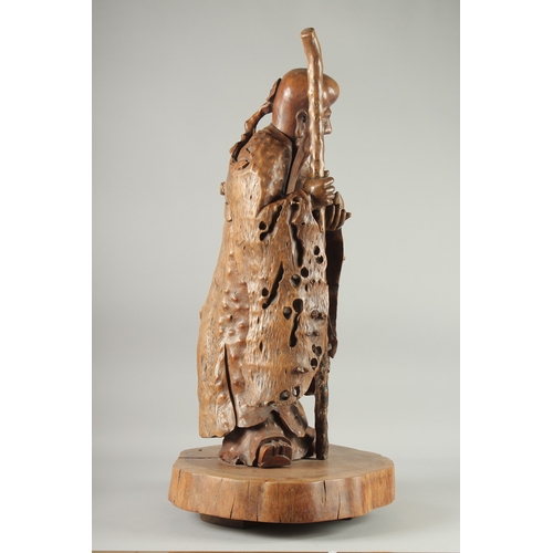 151 - A VERY LARGE AND FINE WOOD CARVING OF SHAO LOU, mounted to a natural tree trunk base, the figure hol... 