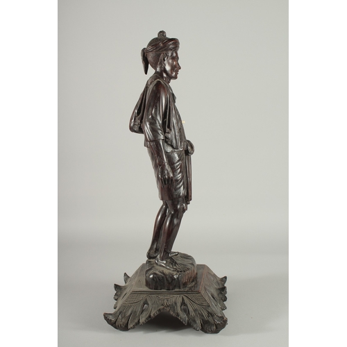 191 - A LARGE INDIAN CARVED HARDWOOD FIGURE, of a man holding a parasol with bone finial, raised and mount... 