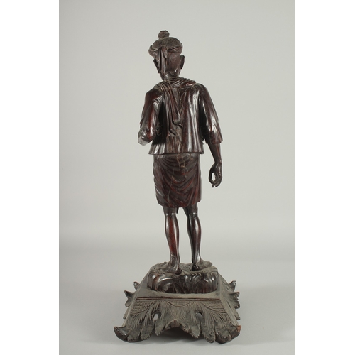 191 - A LARGE INDIAN CARVED HARDWOOD FIGURE, of a man holding a parasol with bone finial, raised and mount... 