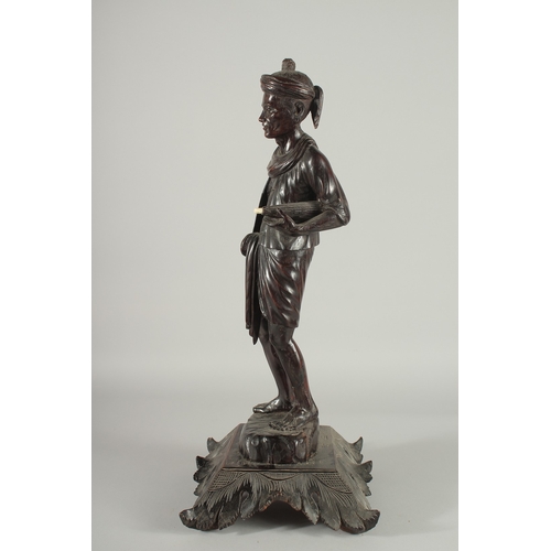 191 - A LARGE INDIAN CARVED HARDWOOD FIGURE, of a man holding a parasol with bone finial, raised and mount... 