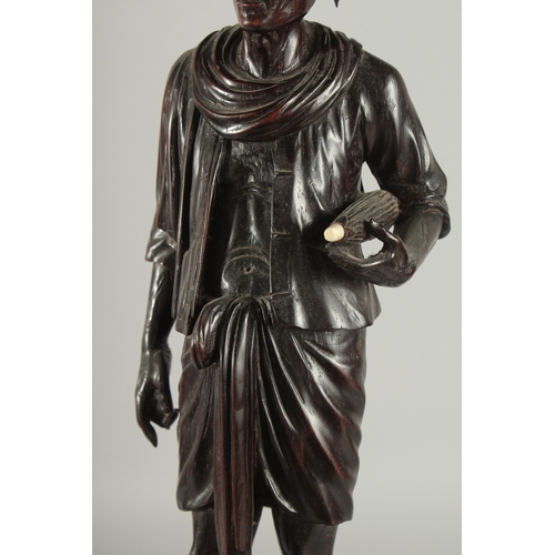 191 - A LARGE INDIAN CARVED HARDWOOD FIGURE, of a man holding a parasol with bone finial, raised and mount... 