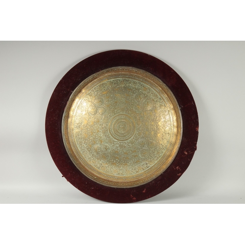 301 - A 19TH CENTURY INDIAN ENGRAVED BRASS TRAY INSET WITHIN A VELVET OVERLAID WOODEN FRAME, beautifully e... 