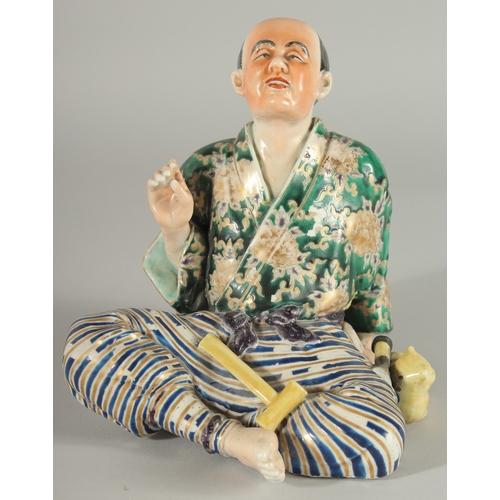 84 - A JAPANESE KUTANI PORCELAIN FIGURE, of a seated man with a cat at his side, 18cm high.