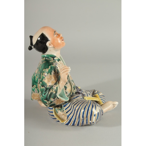 84 - A JAPANESE KUTANI PORCELAIN FIGURE, of a seated man with a cat at his side, 18cm high.