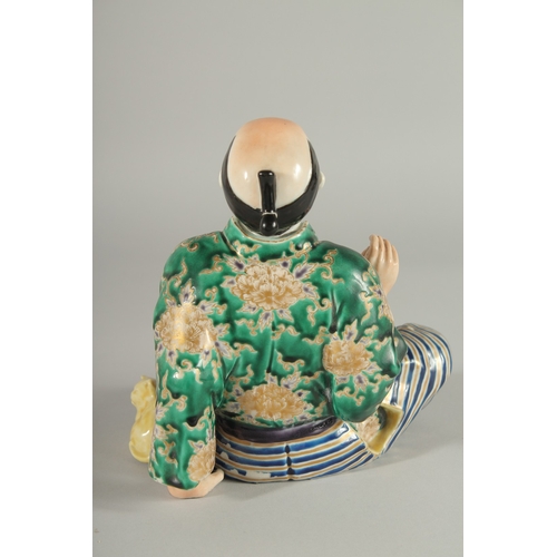 84 - A JAPANESE KUTANI PORCELAIN FIGURE, of a seated man with a cat at his side, 18cm high.