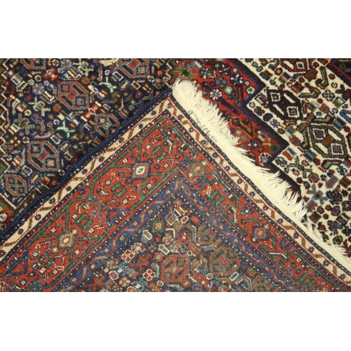 1018 - A PERSIAN WOOL CARPET cream, red and blue ground with all over stylised decoration. 4ft 9ins x 4ft 1... 