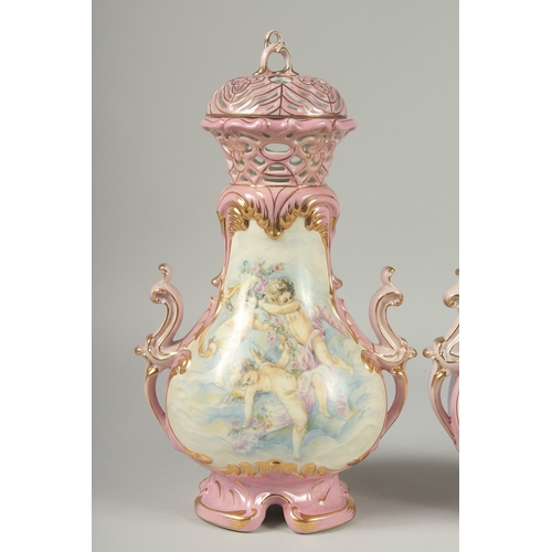 1084 - A PAIR OF SEVRES DESIGN PINK GROUND PORCELAIN VASES AND COVERS decorated with cupids. 15ins high.... 