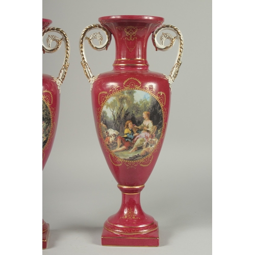 1085 - A PAIR OF SEVRES DESIGN RED GROUND PORCELAIN VASES AND COVERS decorated with reverse scenes of figur... 