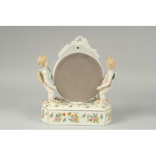 1088 - A SEVRES DESIGN PORCELAIN OVAL MIRROR with two cupids and encrusted with flowers. 11ins high.