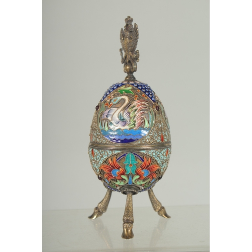 1423 - A LARGE RUSSIAN SILVER AND ENAMEL EGG on three curving feet. 12cm long 5cm diameter decorated with t... 