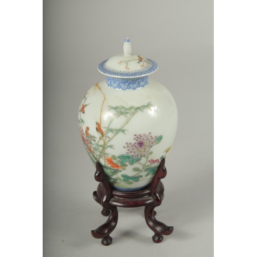 11 - A SMALL CHINESE REPUBLIC PERIOD PORCELAIN JAR AND COVER, on a fitted wooden stand, painted with bird... 