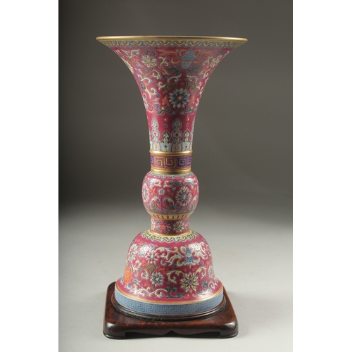 149 - A CHINESE PINK GROUND FAMILLE ROSE PORCELAIN SECTIONAL GU VASE, and fitted hardwood stand, bearing Q... 