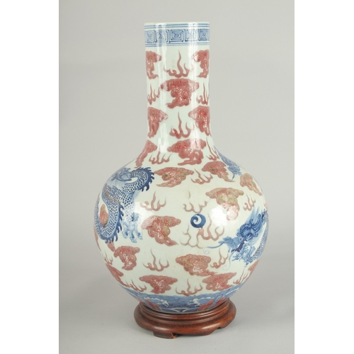 66 - A CHINESE UNDERGLAZE RED AND BLUE PORCELAIN DRAGON VASE ON HARDWOOD STAND, painted with three dragon... 