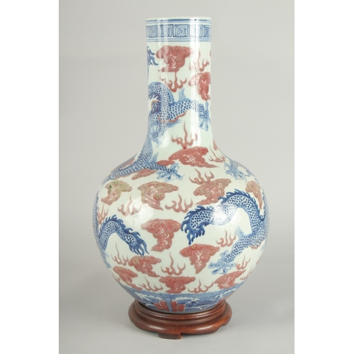 66 - A CHINESE UNDERGLAZE RED AND BLUE PORCELAIN DRAGON VASE ON HARDWOOD STAND, painted with three dragon... 