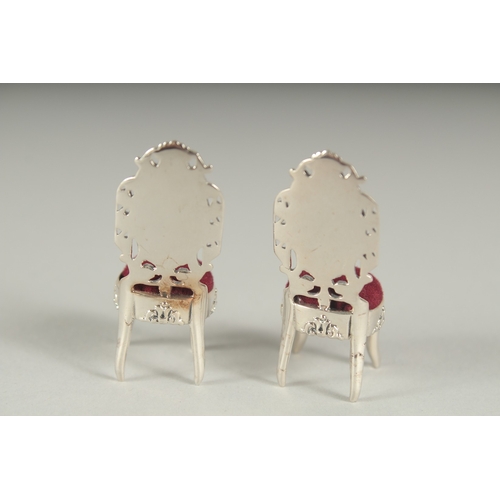 1297 - A SMALL PAIR OF SILVER AND ENAMEL PIN CUSHION CHAIRS.