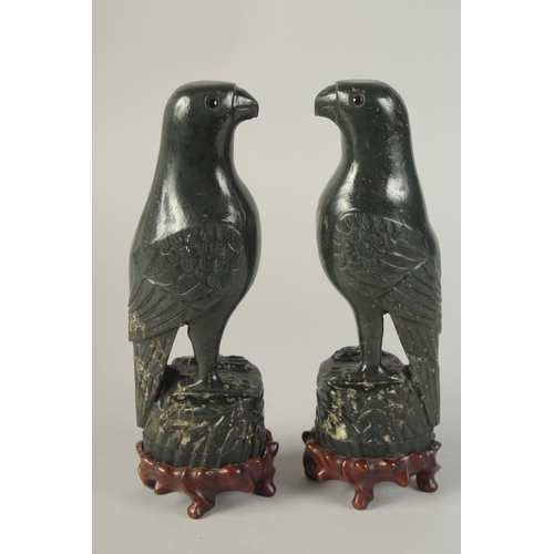 113 - A PAIR OF CHINESE CARVED DARK GREEN HARDSTONE BIRDS, mounted to fitted carved hardwood stands raised... 