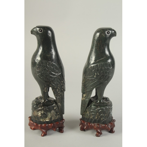113 - A PAIR OF CHINESE CARVED DARK GREEN HARDSTONE BIRDS, mounted to fitted carved hardwood stands raised... 