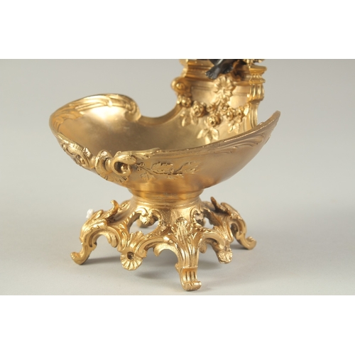 1279 - A BRONZE AND GILT BRONZE TABLE SALT modelled as a cherub, seated on a shell shaped dish. 7ins high.... 