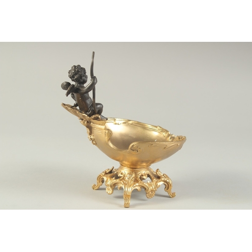 1279 - A BRONZE AND GILT BRONZE TABLE SALT modelled as a cherub, seated on a shell shaped dish. 7ins high.... 