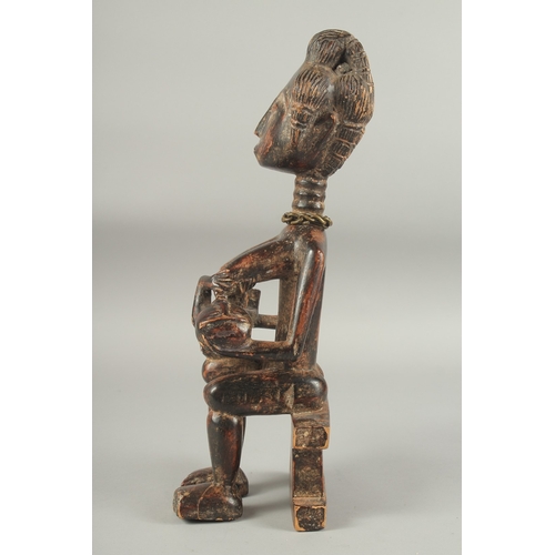 1281 - A CARVED AFRICAN FIGURE OF A WOMAN SITTING ON A BENCH, feeding a baby. 14ins high.