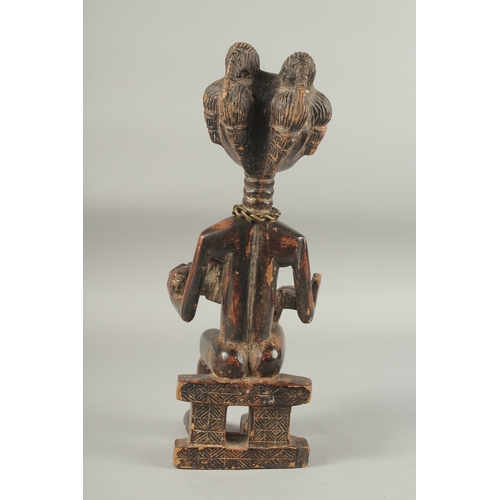 1281 - A CARVED AFRICAN FIGURE OF A WOMAN SITTING ON A BENCH, feeding a baby. 14ins high.