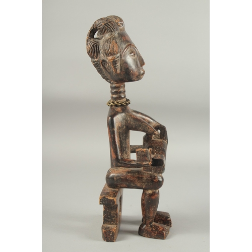 1281 - A CARVED AFRICAN FIGURE OF A WOMAN SITTING ON A BENCH, feeding a baby. 14ins high.