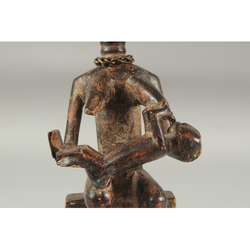 1281 - A CARVED AFRICAN FIGURE OF A WOMAN SITTING ON A BENCH, feeding a baby. 14ins high.