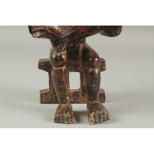 1281 - A CARVED AFRICAN FIGURE OF A WOMAN SITTING ON A BENCH, feeding a baby. 14ins high.