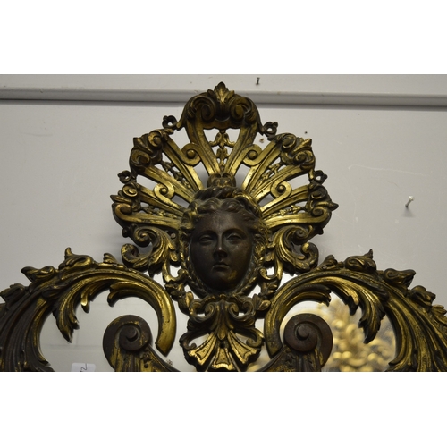 310 - A highly ornate brass over-mantel mirror with female mask, swags, C scrolls etc.