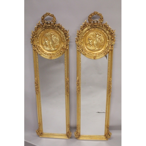 1010 - A TALL PAIR OF NARROW GILT MIRRORS with classical circular panels and garlands. 5ft 9ins high x 1ft ... 