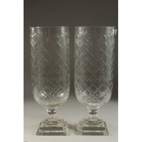 1053 - A PAIR OF GLASS STORM LANTERNS on square stepped bases. 16ins high.