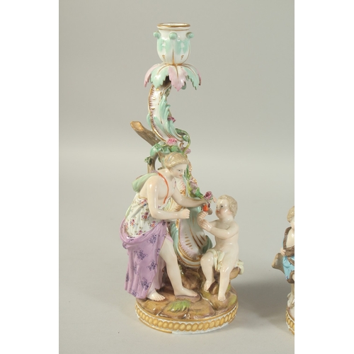 1076 - A PAIR OF MEISSEN CANDLESTICKS depicting winter and spring. 29cm high.  Cross swords mark in blue.... 