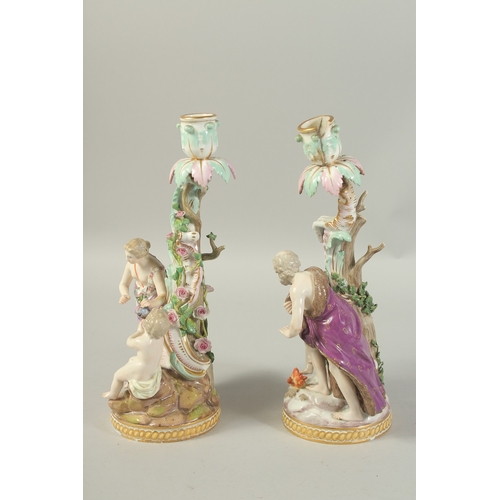 1076 - A PAIR OF MEISSEN CANDLESTICKS depicting winter and spring. 29cm high.  Cross swords mark in blue.... 