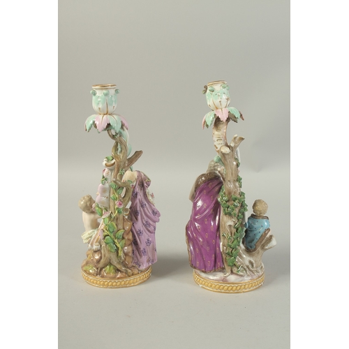 1076 - A PAIR OF MEISSEN CANDLESTICKS depicting winter and spring. 29cm high.  Cross swords mark in blue.... 