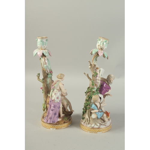 1076 - A PAIR OF MEISSEN CANDLESTICKS depicting winter and spring. 29cm high.  Cross swords mark in blue.... 