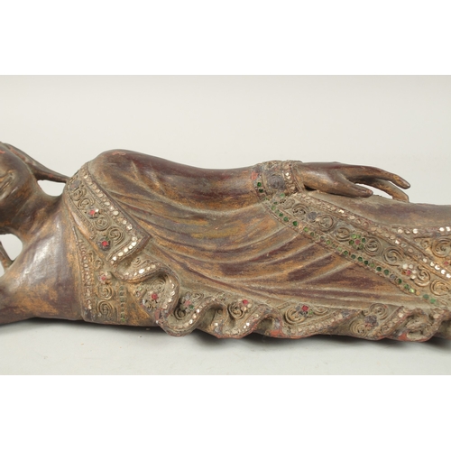 379 - AN INDIAN CARVED WOOD RECLINING BUDDHA, with inset coloured glass to the robes, 59cm long.