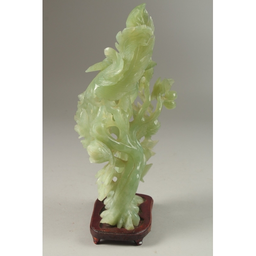 5 - A CHINESE CARVED JADE GROUP ON HARDWOOD STAND, carved with a peacock elevated on a large floral reli... 