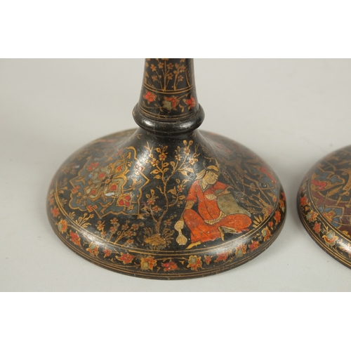 315 - A PAIR OF PERSIAN QAJAR LACQUERED WOOD CANDLESTICKS, decorated with figures and flora, 26.5cm high.