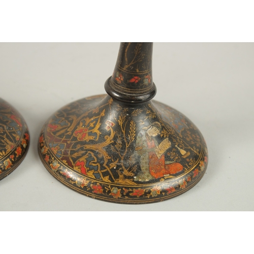 315 - A PAIR OF PERSIAN QAJAR LACQUERED WOOD CANDLESTICKS, decorated with figures and flora, 26.5cm high.