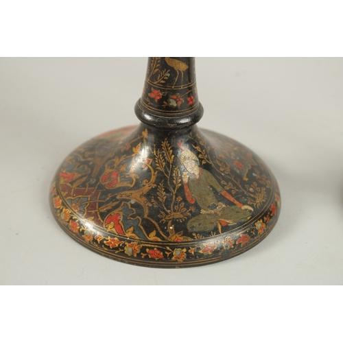 315 - A PAIR OF PERSIAN QAJAR LACQUERED WOOD CANDLESTICKS, decorated with figures and flora, 26.5cm high.